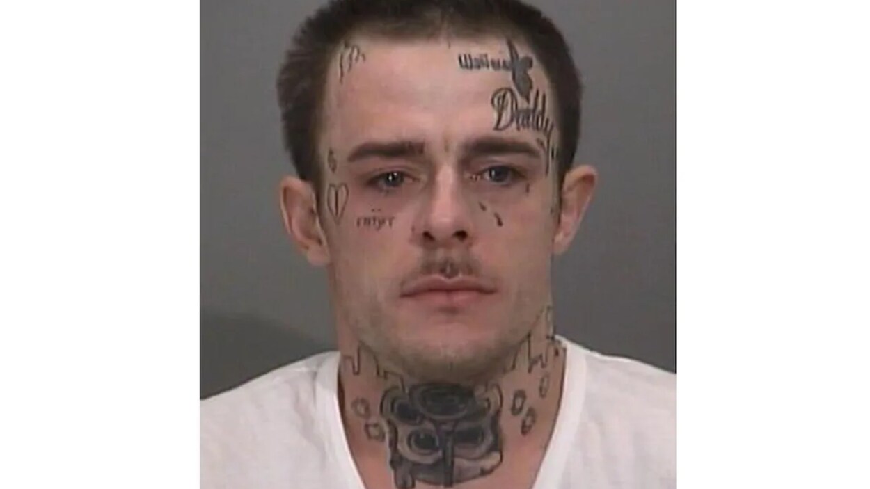 Une photo d'un homme blanc avec des tatouages sur le visage et le cou.