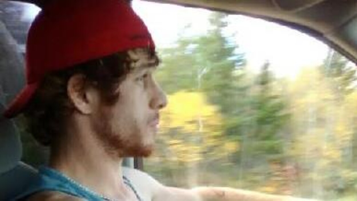 Un homme tatoué et barbu coiffé d'une casquette vu de profil au volant d'une voiture Un homme tatoué et barbu coiffé d'une casquette vu de profil au volant d'une voiture