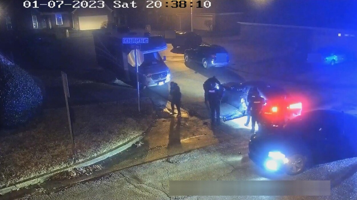 Capture d'écran d'une vidéo de surveillance montrant une jeune homme noir au sol, accoté contre une voiture de police.