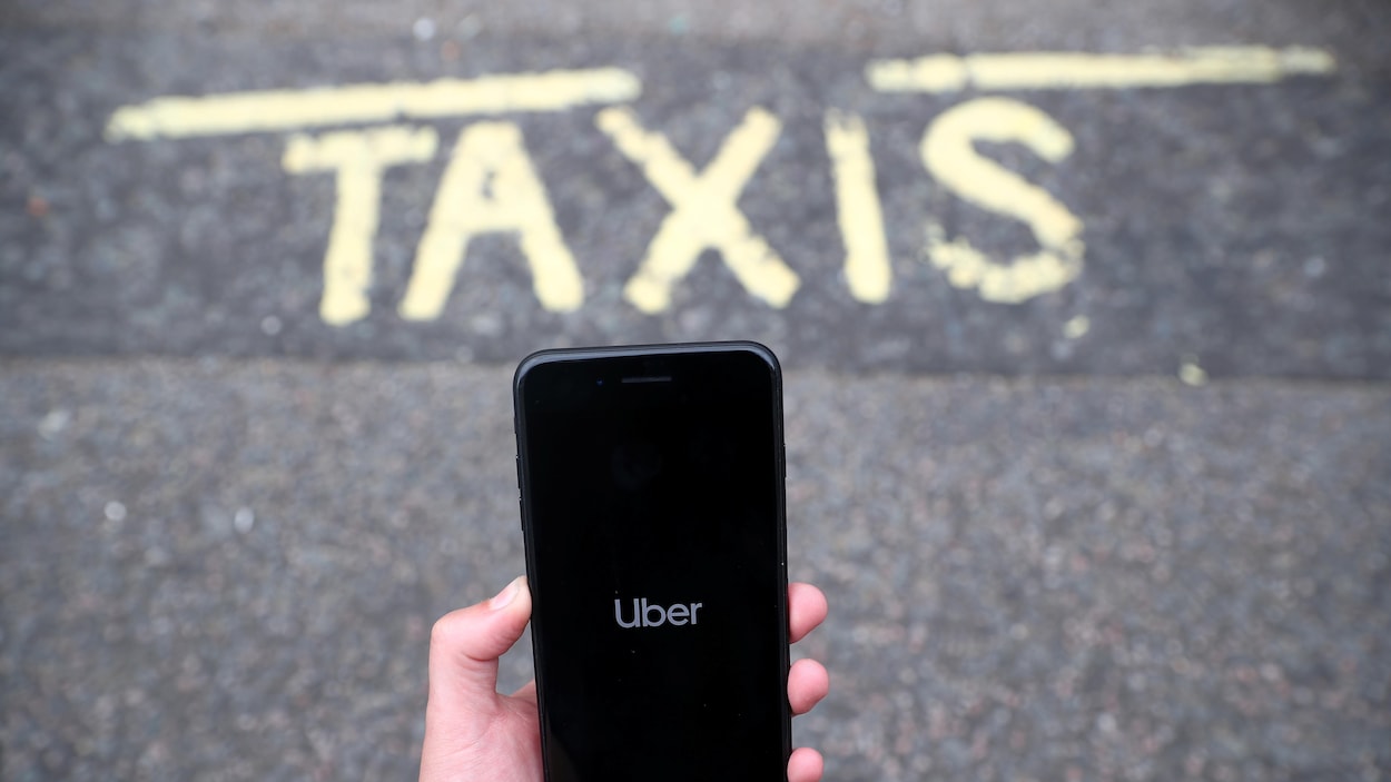 Un téléphone intelligent affichant l'application Uber, au-dessus d'une chaussée sur laquelle il est écrit : « TAXIS ».