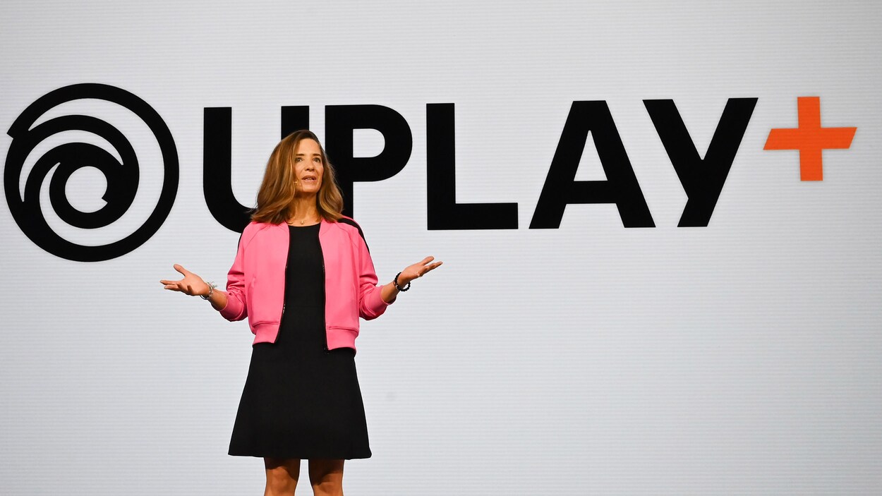 Une femme sur scène devant un écran géant affichant le logo du service Uplay+.