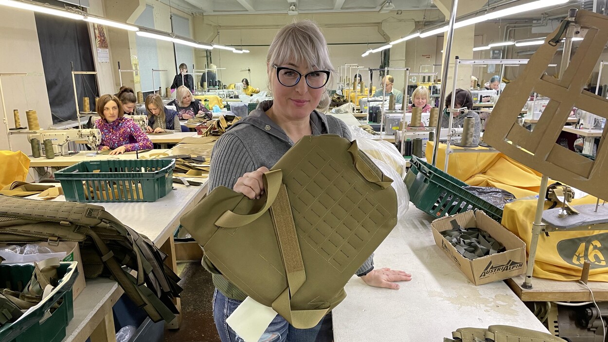 Une femme dans une usine tenant un gilet pare-balles.