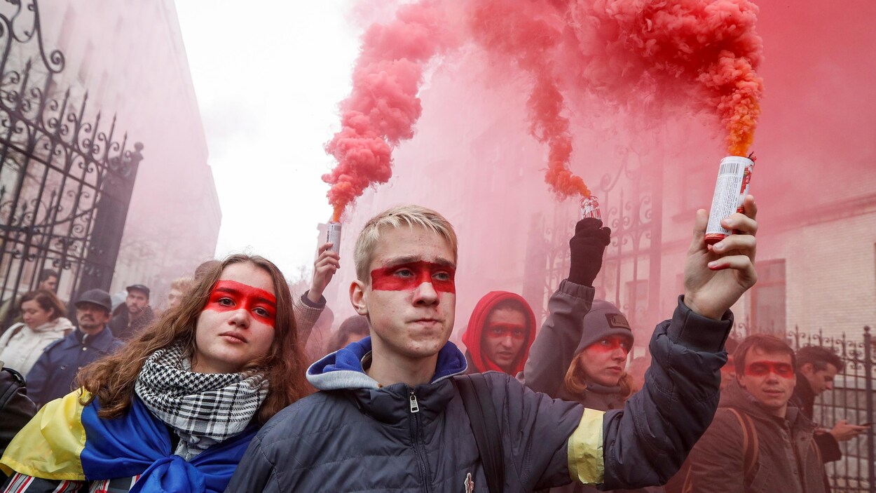 Plusieurs manifestants, dont les yeux sont maquillés d'un bandeau rouge, tiennent des bombes fumigènes.