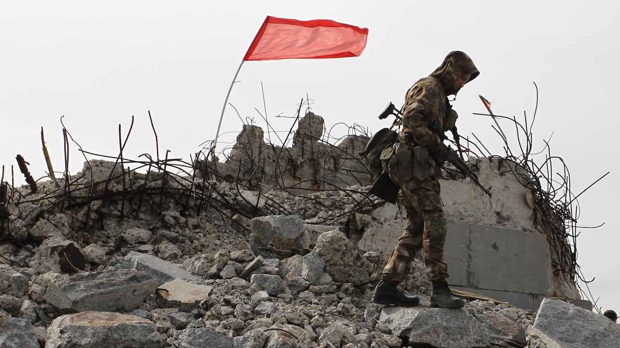 Un soldat monte la garde sur les ruines d'un bâtiment où flotte un drapeau.