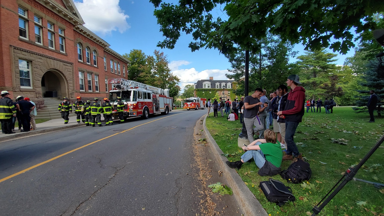 Pompiers devant un édifice et étudiants évacués sur la pelouse de l'autre côté de la rue.