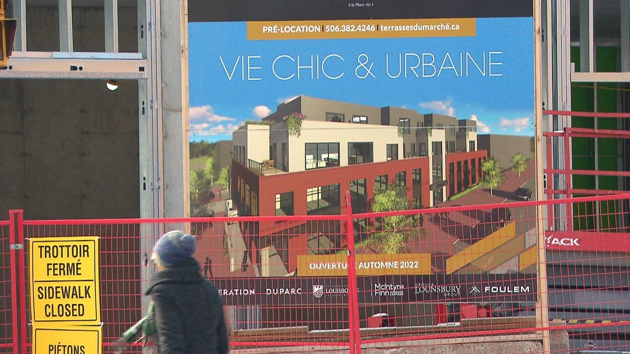 Une femme passe devant un chantier qui annonce une « vie chic et urbaine »