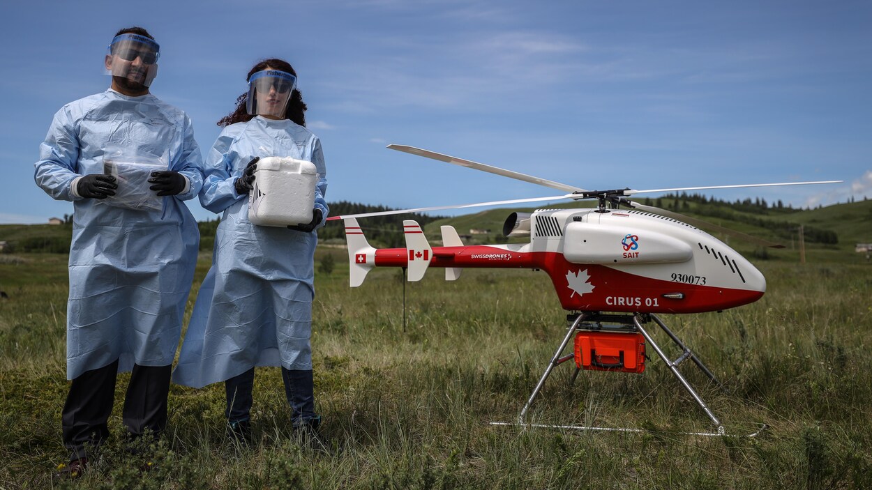 Du personnel médical en équipements de protection individuelle à côté d'un drone dans un champ.