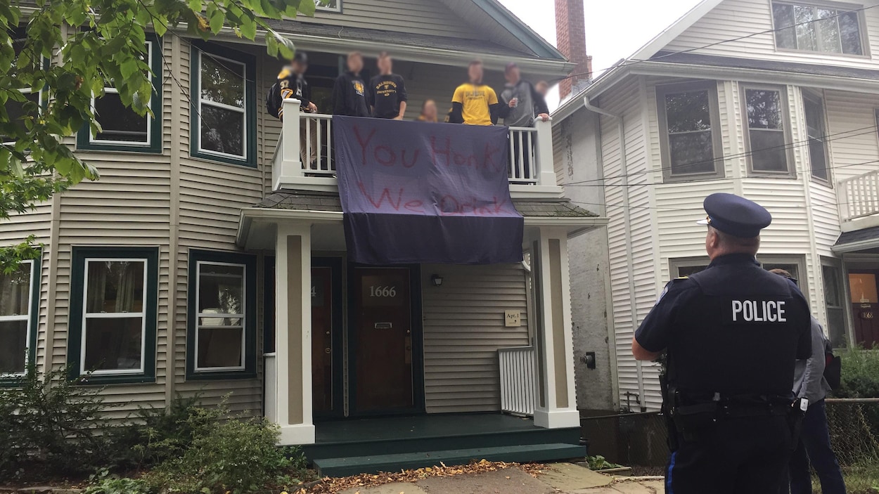 Des policiers sur le trottoir discutent avec des jeunes qui se trouvent sur un balcon à l'étage d'une maison.