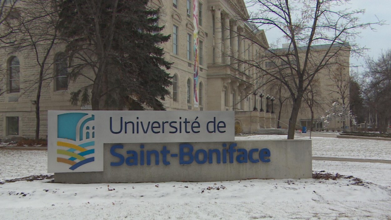 Une grande enseigne indique « Université de Saint-Boniface ». Sur le sol, on voit de la neige. En arrière-plan un grand édifice de pierre.