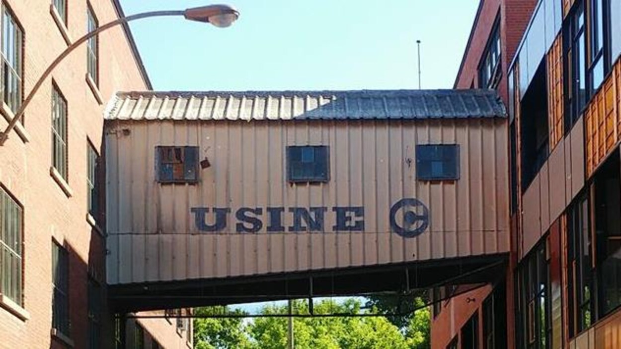 Une passerelle entre deux bâtiments sur laquelle il a été peinturé « Usine C ».