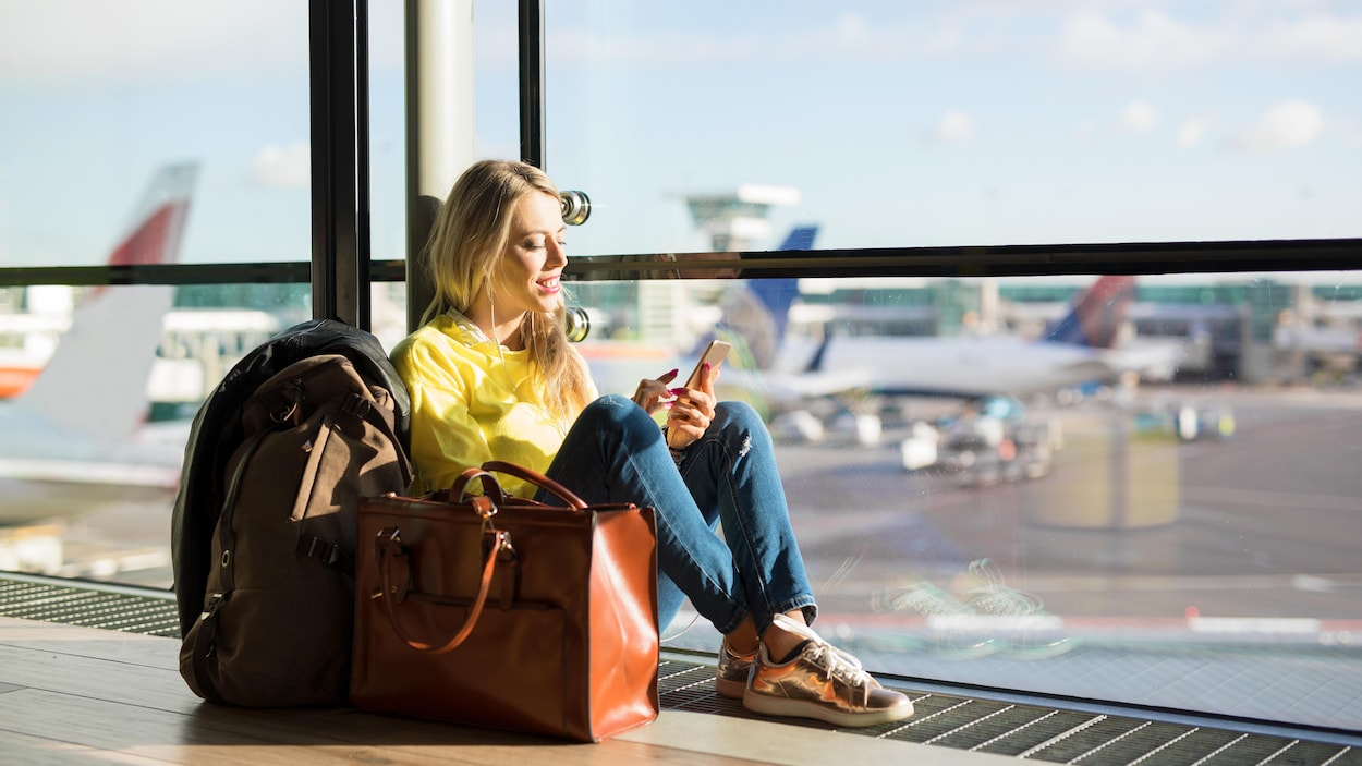 Une femme consulte son téléphone cellulaire en attendant son vol à l'aéroport. Une femme consulte son téléphone cellulaire en attendant son vol à l'aéroport.