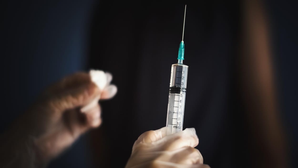 Une main gantée tient une seringue qui contient un vaccin.
