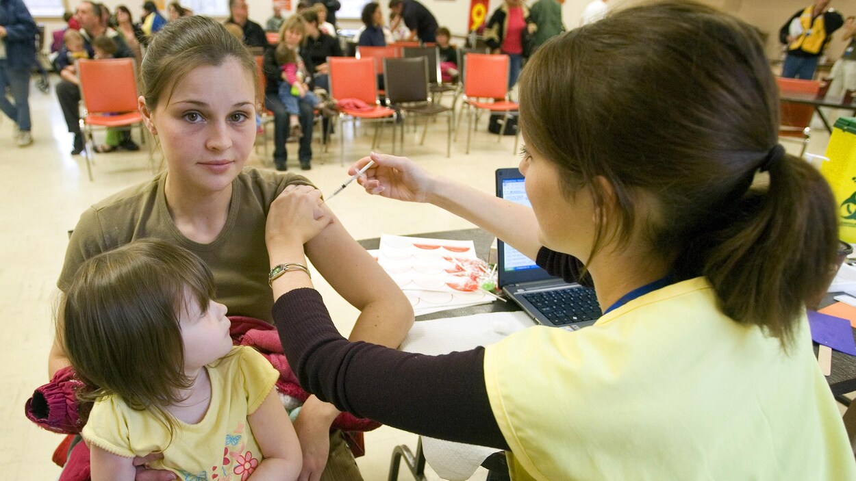 Une jeune femme, sa petite fille d'environ 4 ans sur ses genoux, reçoit le vaccin administré par une infirmière.
