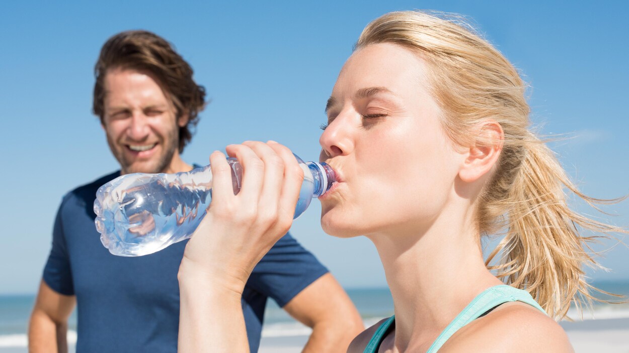 Un homme regarde une femme boire l'eau d'une bouteille.