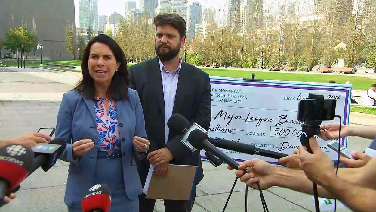 La candidate à la mairie Valérie Plante, en compagnie du porte-parole de Projet Montréal en matière de grands événements sportifs, Éric Alan Caldwell, devant un « chèque en blanc » géant à la Major League Baseball avec la fausse signature de Denis Coderre, lors d'une conférence de presse.