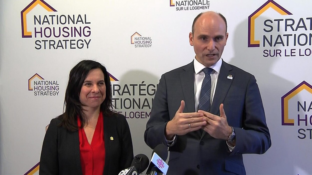 Les deux politiciens sont debout devant un panneau sur lequel est écrit « Stratégie nationale sur le logement ». Valérie Plante sourit pendant que Jean-Yves Duclos donne des explications.
