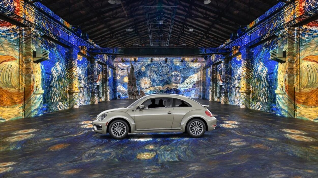Une voiture au milieu d'un hangar désert. Des œuvres de Van Gogh sont projetées sur le sol et sur les murs.