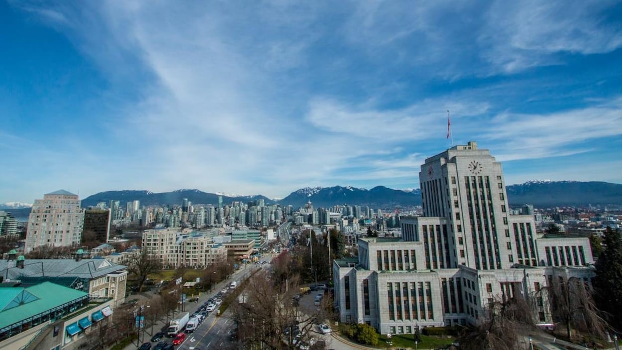 L’hôtel de ville de Vancouver en premier plan, avec le centre-ville derrière et les montagnes de la rive nord en arrière-plan.