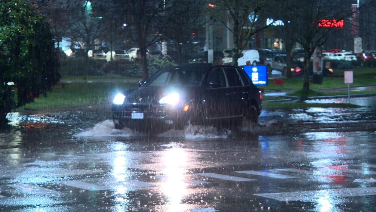 Une voiture dans une flaque d'eau, lumières allumées, de la pluie brouille la photo, stationnement en arrière-plan.