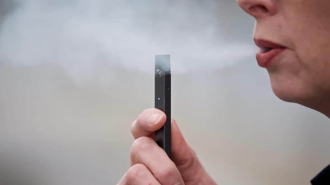 De la vapeur s'échappe de la bouche d'une femme qui tient une cigarette électronique dans une main.