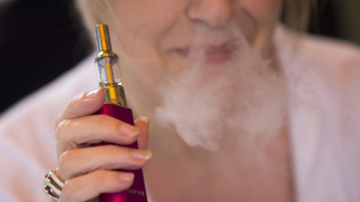 Une femme fume une cigarette électronique.