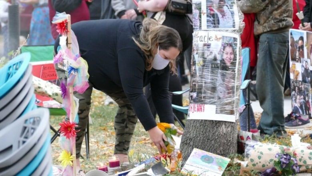 Une femme endeuillée dépose des fleurs près d'un arbre où l'on voit des photos de Jennifer Dethmers.