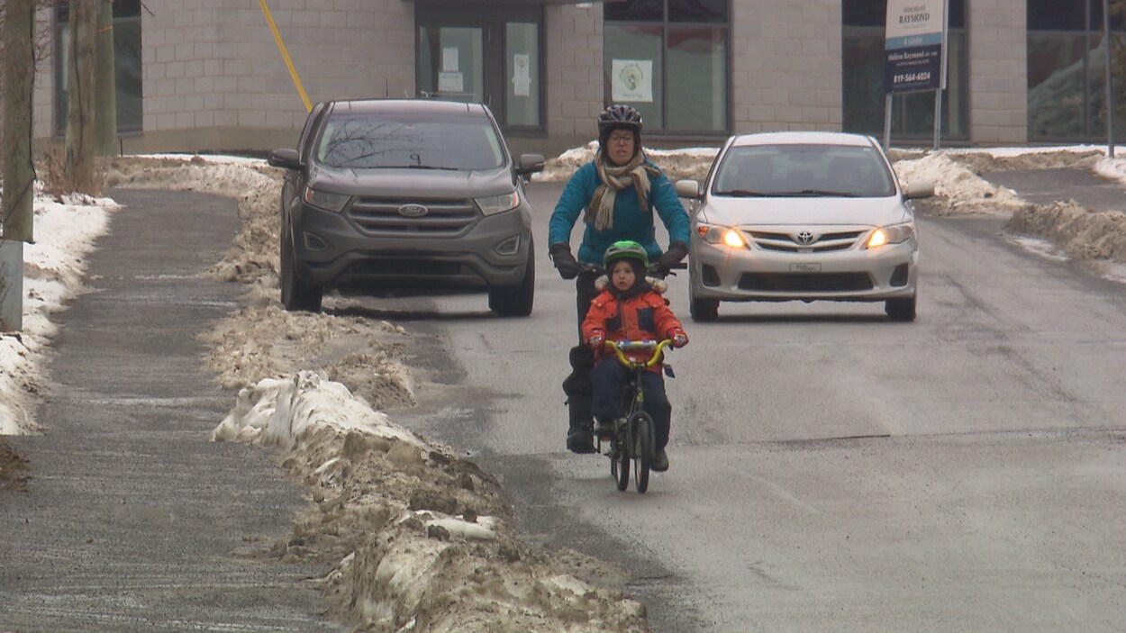 Une cycliste et son garçon partagent la route avec une voiture qui les suit de près