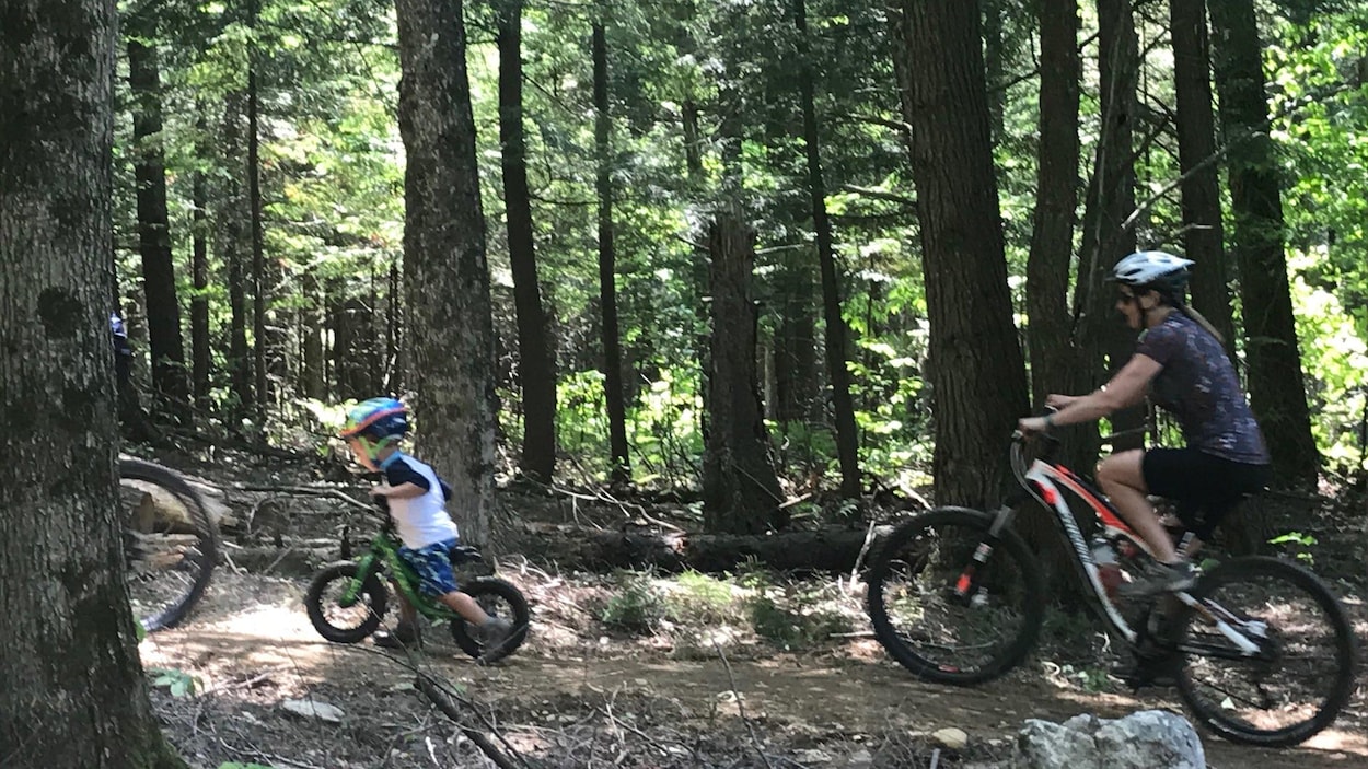 Un jeune garçon sur son vélo suivi d'une femme, aussi à vélo sur un sentier