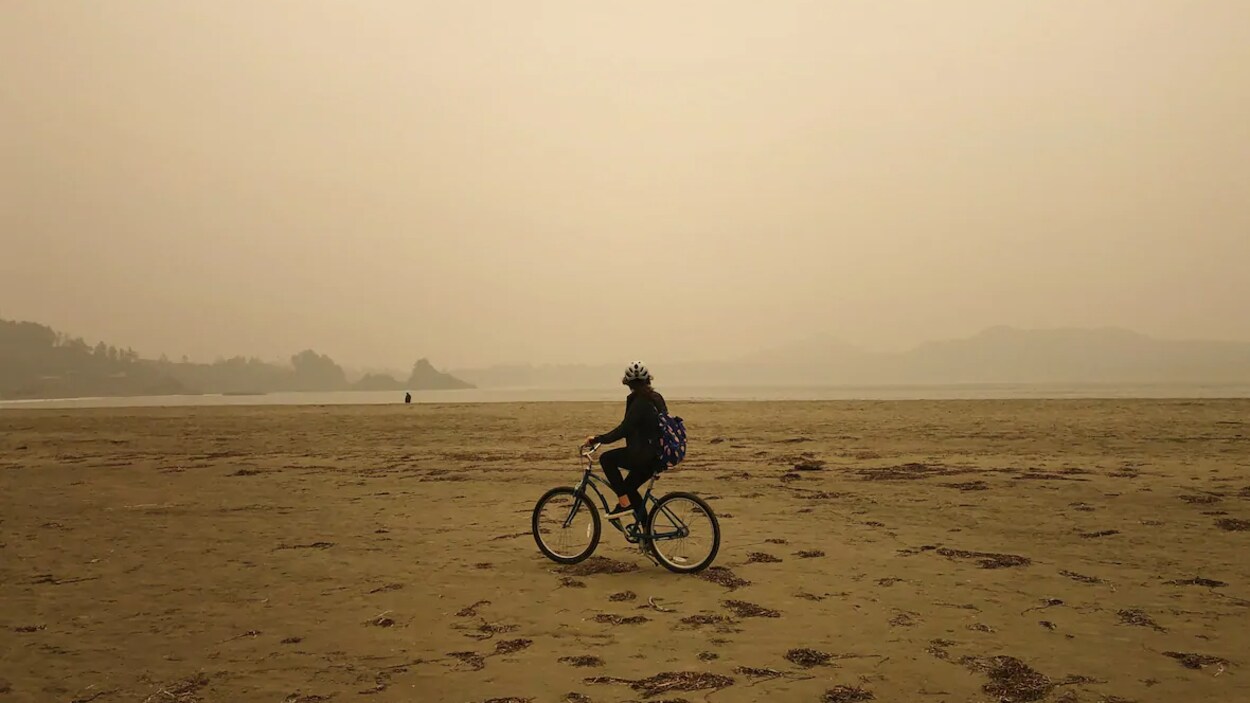 Un cycliste portant un sac à dos et un casque pédale dans la fumée sur une grande plage de Tofino, en Colombie-Britannique.