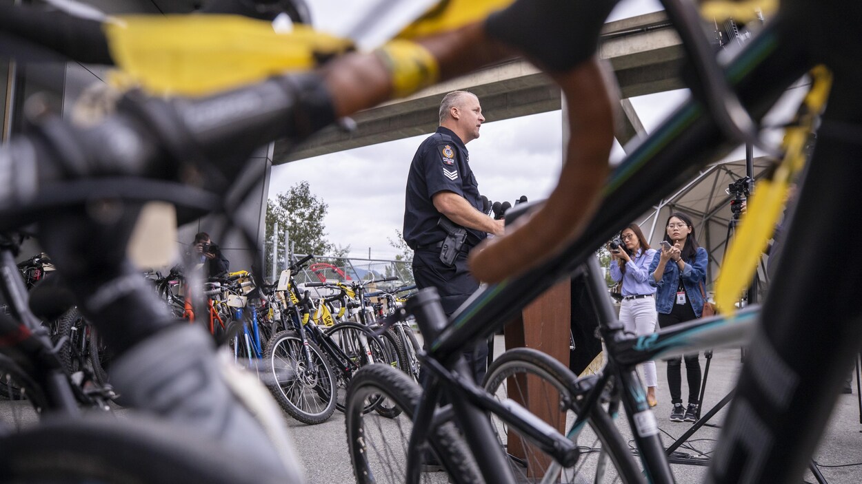 Le policier Aaron Roed parle aux médias debout lors de son annonce de la saisie de 148 vélos à Vancouver pendant que des journalistes l'écoutent.