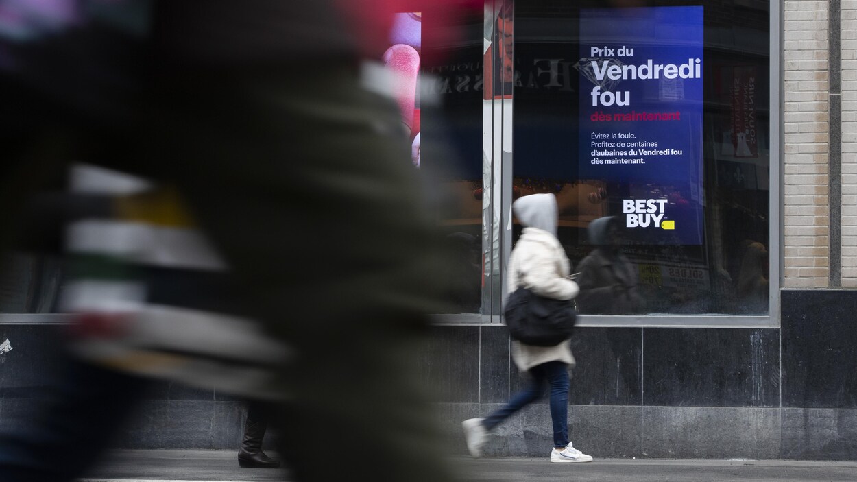 Des passants devant une vitrine de magasin où sont affichés des soldes.