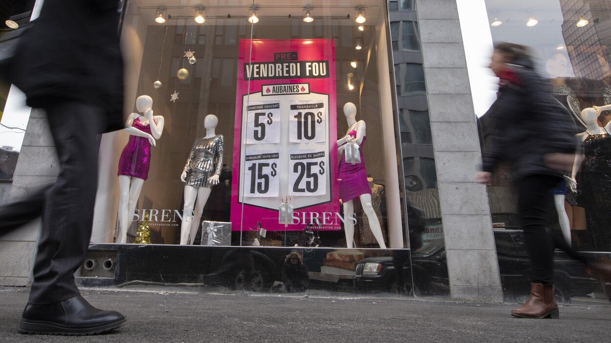 Des passants devant une vitrine de magasin où sont affichées des soldes.
