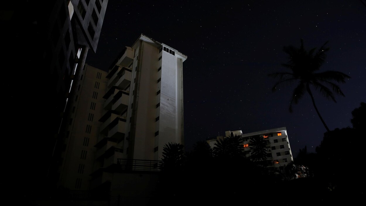 Des immeubles d'habitation sont dans le noir. De faibles lueurs apparaissent à seulement quatre fenêtres.