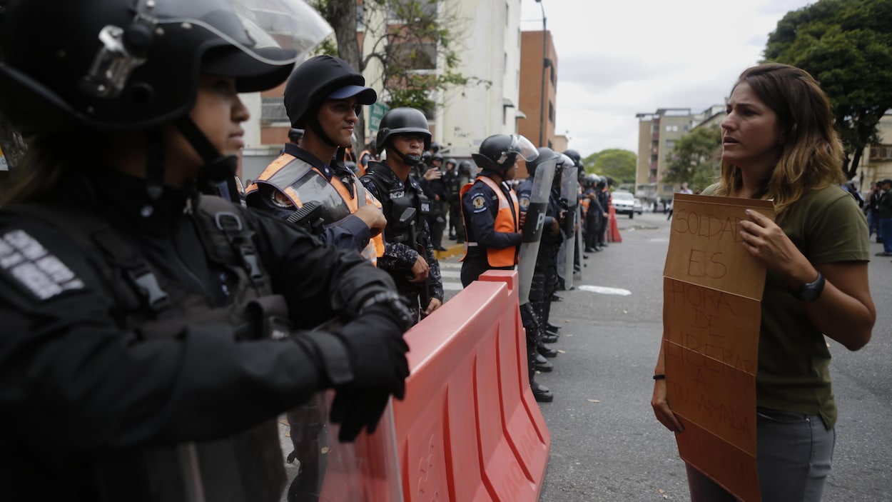 Une femme portant une affiche devant elle s'adresse à une ligne de policiers en tenue antiémeute dans une rue de la capitale.