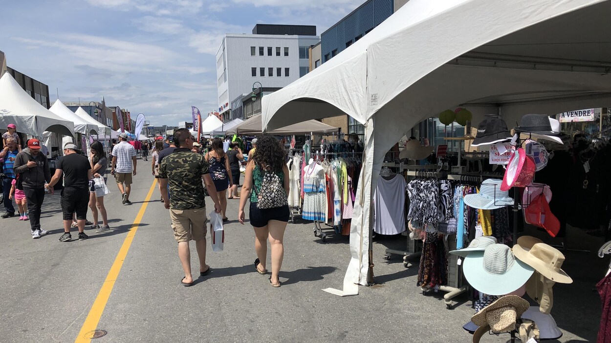 Des clients marchent entre les kiosques des magasins lors d'une vente trottoir.