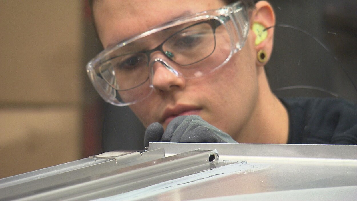 Une femme qui porte des lunettes protectrices inspecte une feuille de métal dans une usine. Une femme qui porte des lunettes protectrices inspecte une feuille de métal dans une usine.