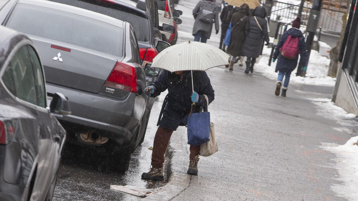 Un homme avec un parapluie tente de garder son équilibre sur une chaussée glissante.