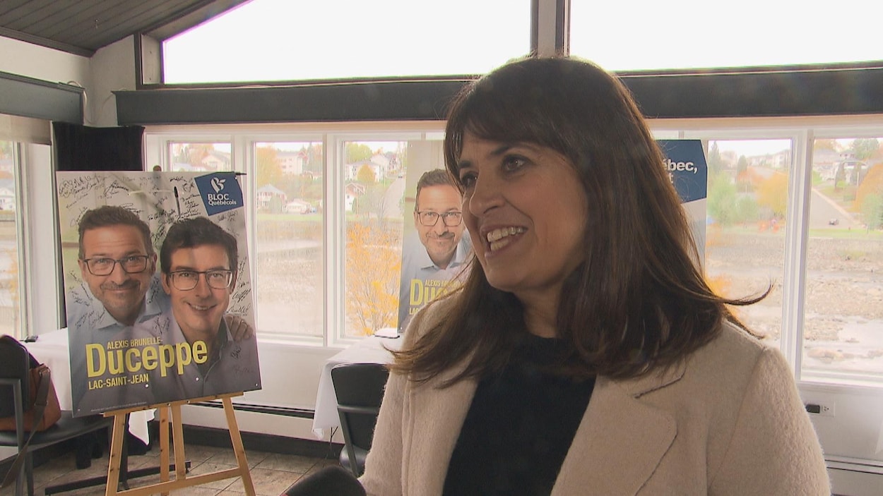 Une femme devant une pancarte électorale.
