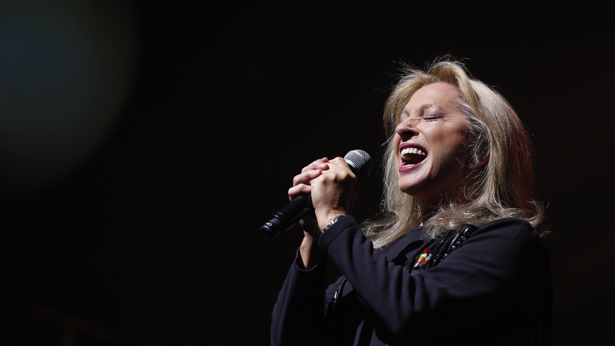 La chanteuse française Véronique Sanson tient son micro à deux mains et chante en fermant les yeux.