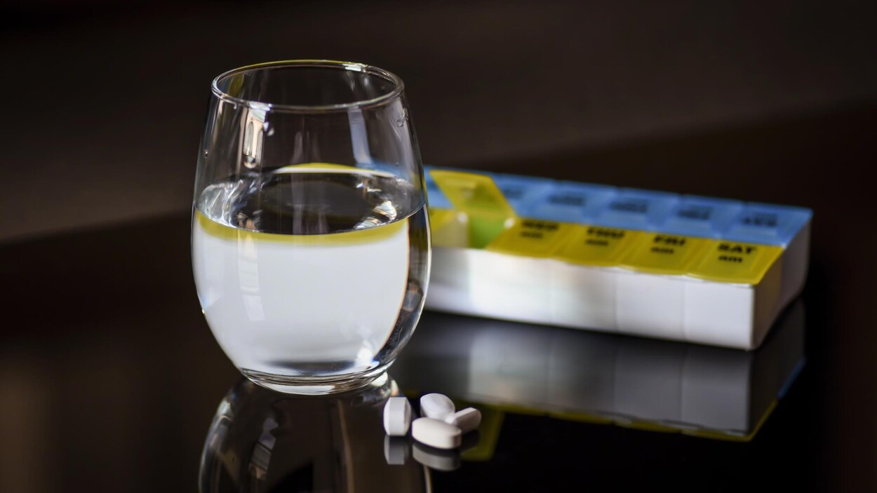 Un verre d'eau et des pilules sur une table.