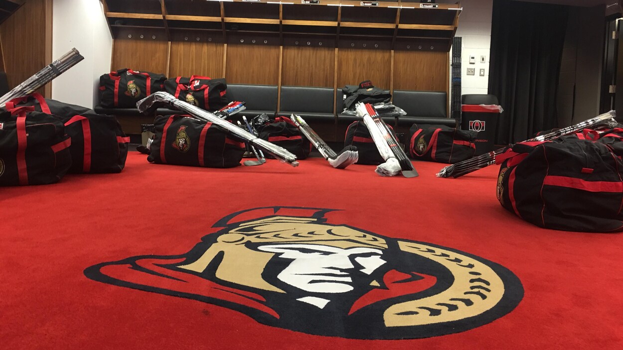 Un vestiaire de hockey avec des sacs et des bâtons au sol.