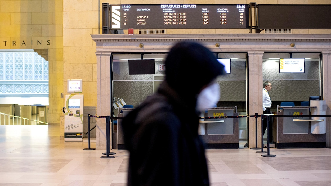 Un homme masqué passe devant un comptoir de VIA Rail à la gare Union de Toronto.