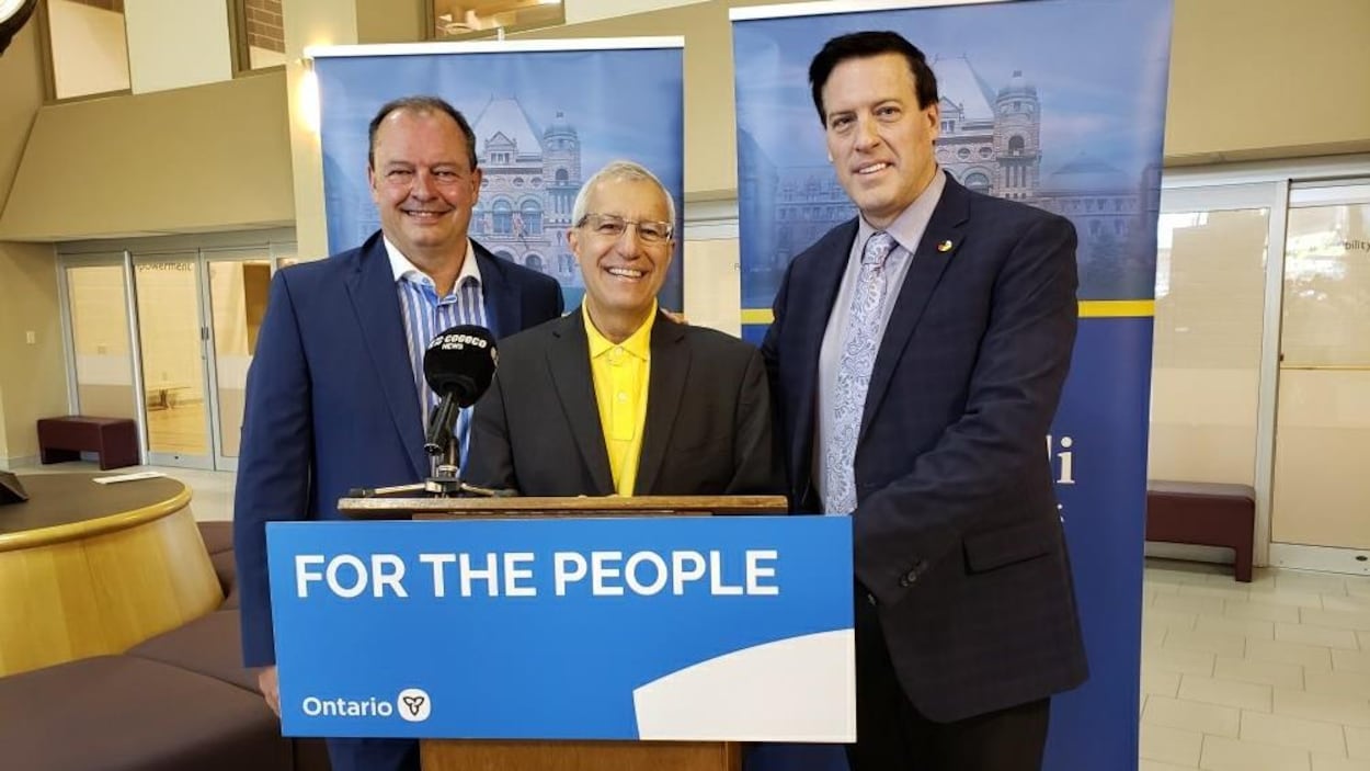 Vic Fedeli pose devant un podium lors d'une conférence de presse.