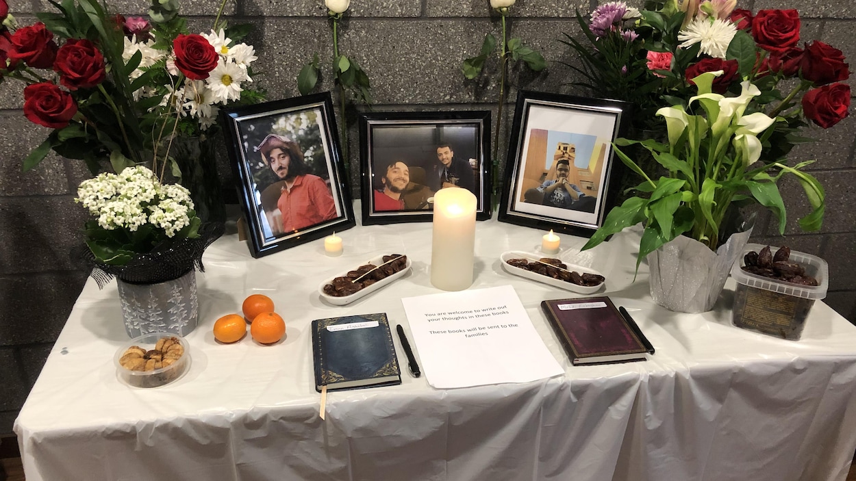 Des portrait des hommes avec des chandelles, des fleurs et des denrées sont installés sur une table avec une nappe blanche.