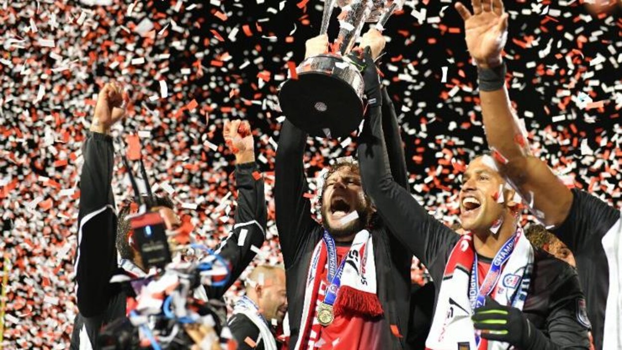 Des joueurs tout sourire brandissent la coupe sous une pluie de confettis. Des joueurs tout sourire brandissent la coupe sous une pluie de confettis.