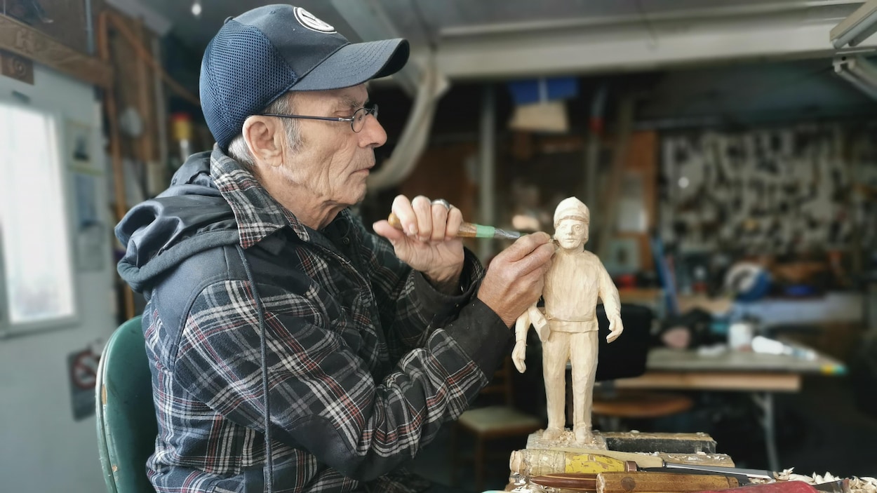 Victor Dallaire taille le corps d'un homme dans une pièce de bois.