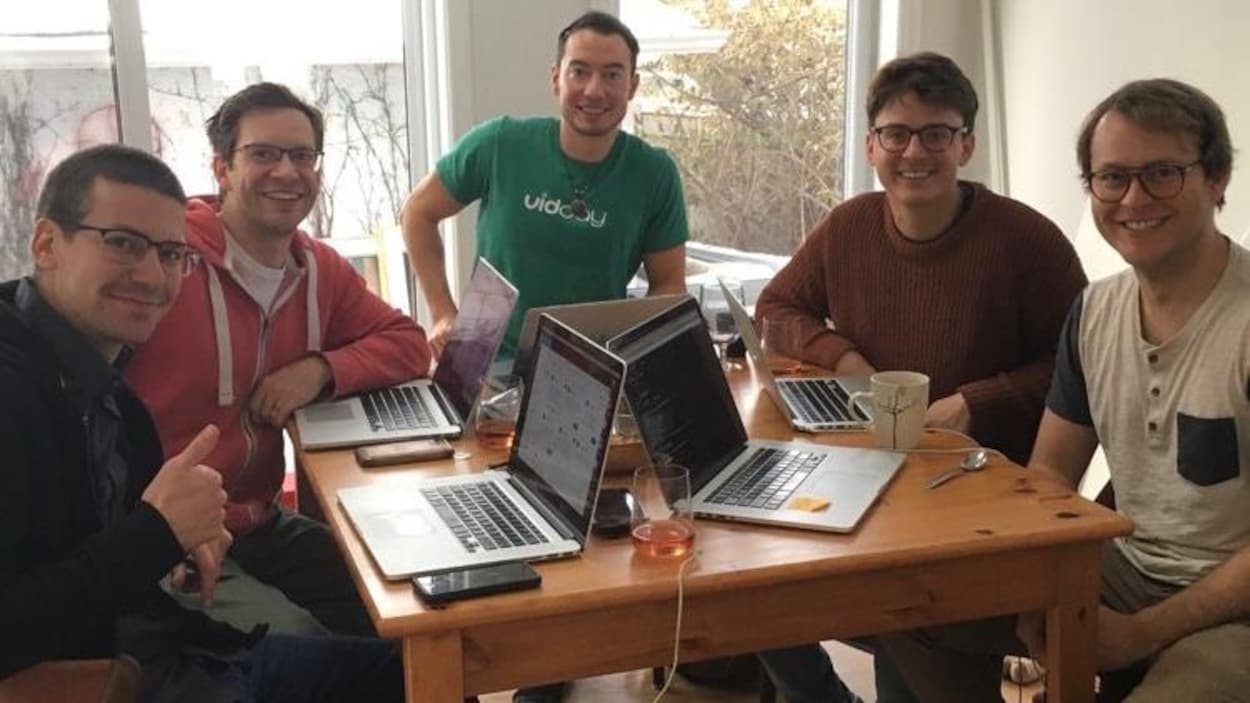 Les membres de l'équipe de VidDay assis autour d'une table travaillent chacun à leur ordinateur.