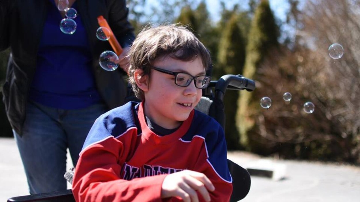 Un petit garçon qui porte des lunettes est assis dans un fauteuil roulant.