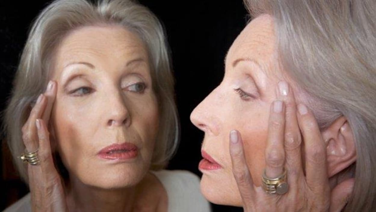 Une femme se regarde le visage dans un miroir.