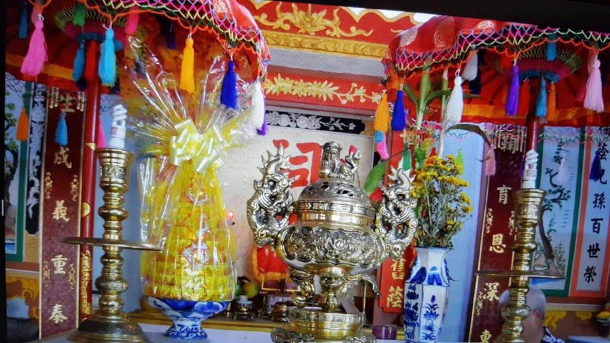 Un autel des ancêtres multicolores dans lequel sont placés un pot de fleur et objets décoratifs dont des bougies